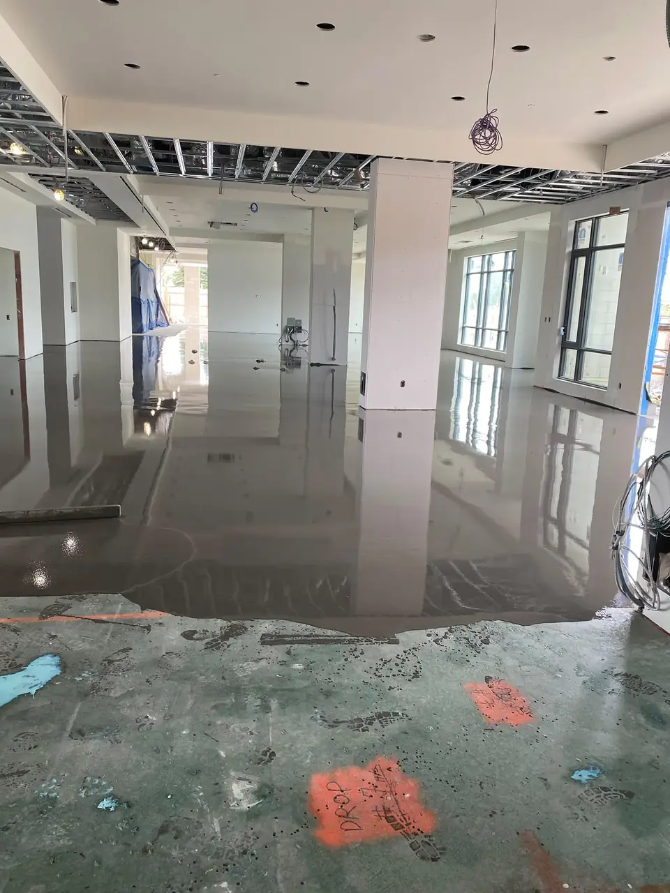 Self-leveling concrete advancing across a large primed commercial floor with layout marks