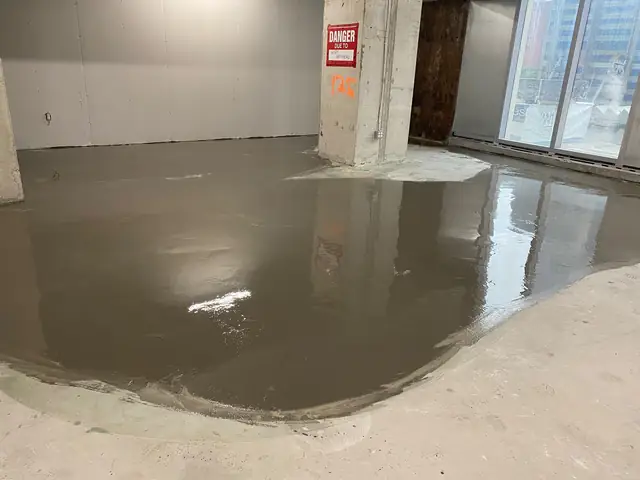 Self-leveling concrete poured on a commercial construction site beside a danger overhead sign