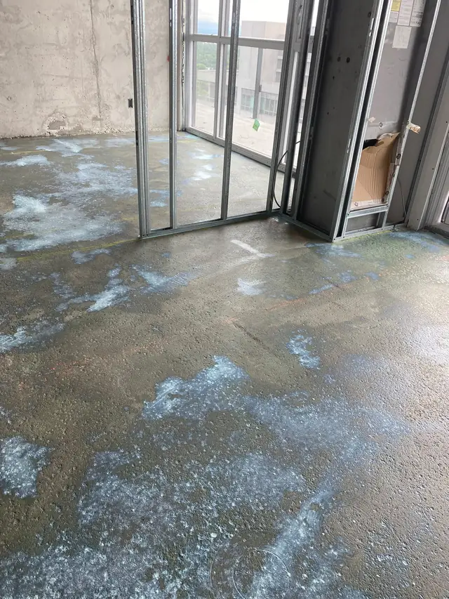 Rough high-rise condo concrete slab with residue beside floor-to-ceiling windows before leveling