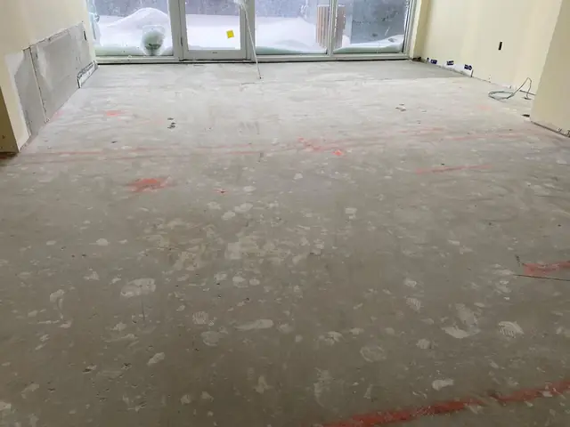 Uneven concrete floor before leveling, with spray-paint elevation marks on the slab