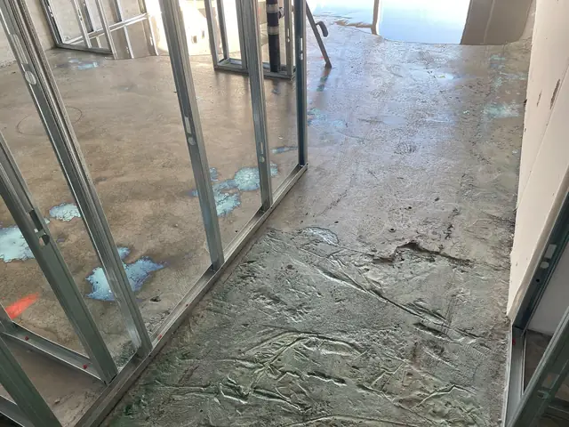 Damaged concrete slab with rough patches between metal stud walls in a condo under construction
