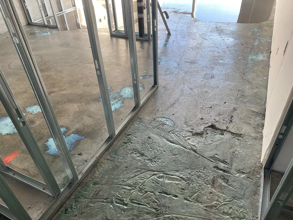 Damaged concrete slab with rough patches between metal stud walls in a condo under construction