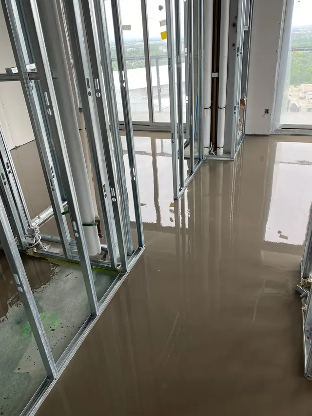 Wet self-leveling concrete poured between metal stud partitions in a high-rise condo unit