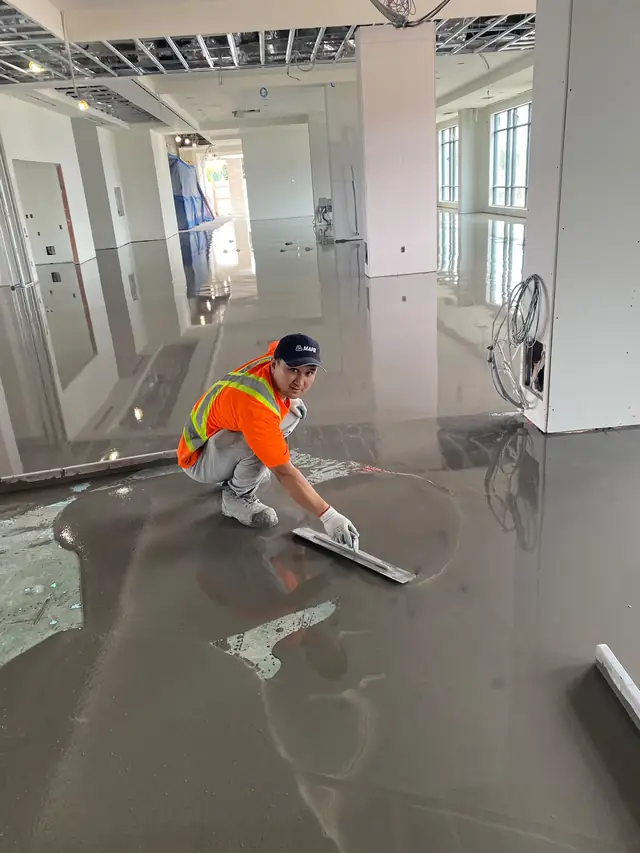 MIR installer kneeling to trowel self-leveling concrete at the edge of a commercial floor