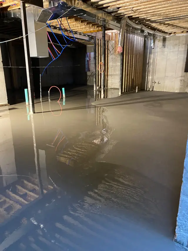 Wet self-leveling concrete in a basement reflecting the ceiling joists and ductwork above