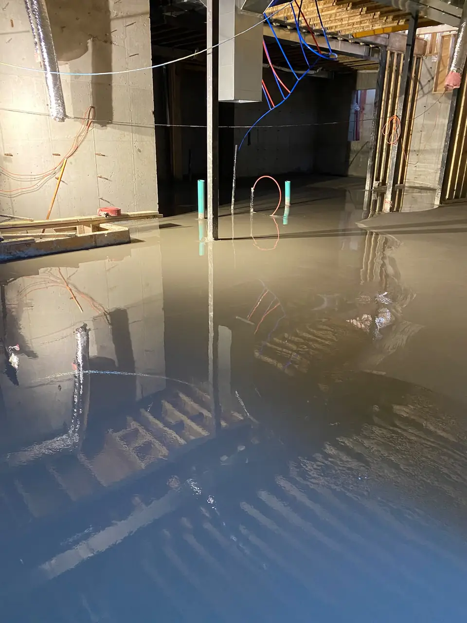 Basement concrete floor leveling in progress with self-leveling underlayment spread across the slab