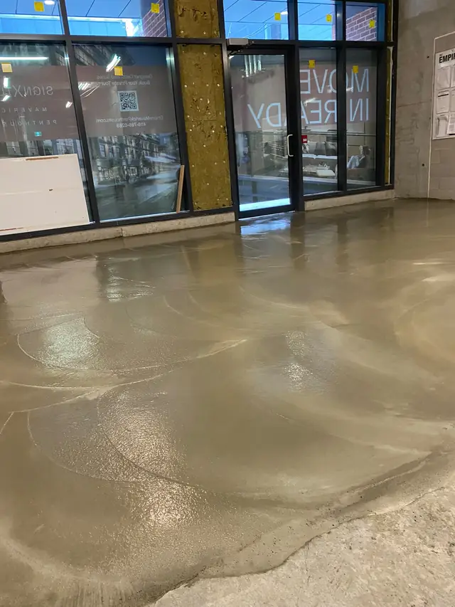 Wet self-leveling concrete in a ground-floor retail unit behind storefront glass
