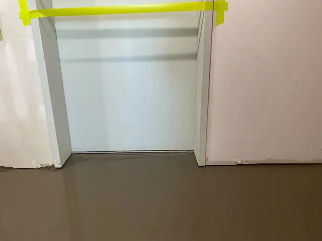 Self-leveling concrete stopped cleanly at a doorway protected with yellow masking tape