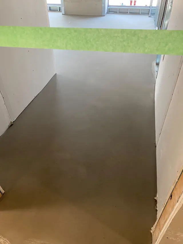 Cured, flat self-leveling concrete floor in a hallway with painter's tape protecting the walls