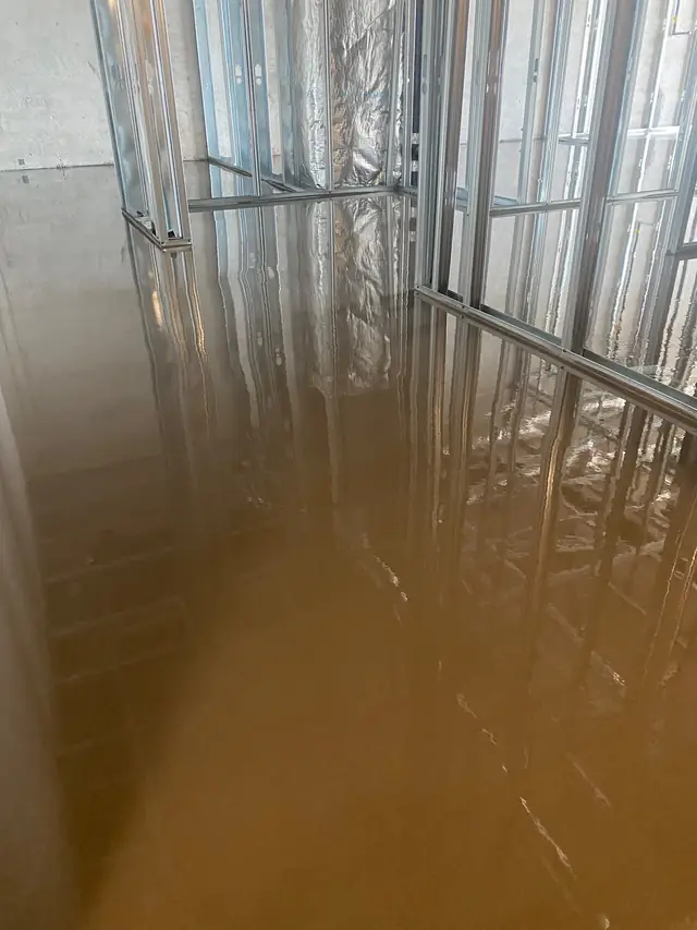 Freshly poured self-leveling concrete in a condo unit with steel stud framing, lit in warm light