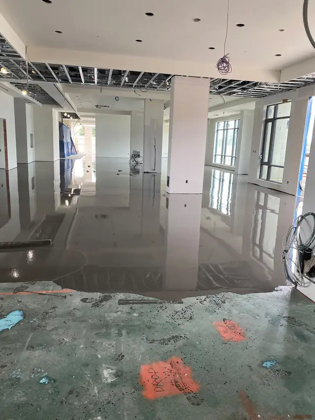 Wet self-leveling concrete meeting the unpoured section of a commercial slab marked with depth notes